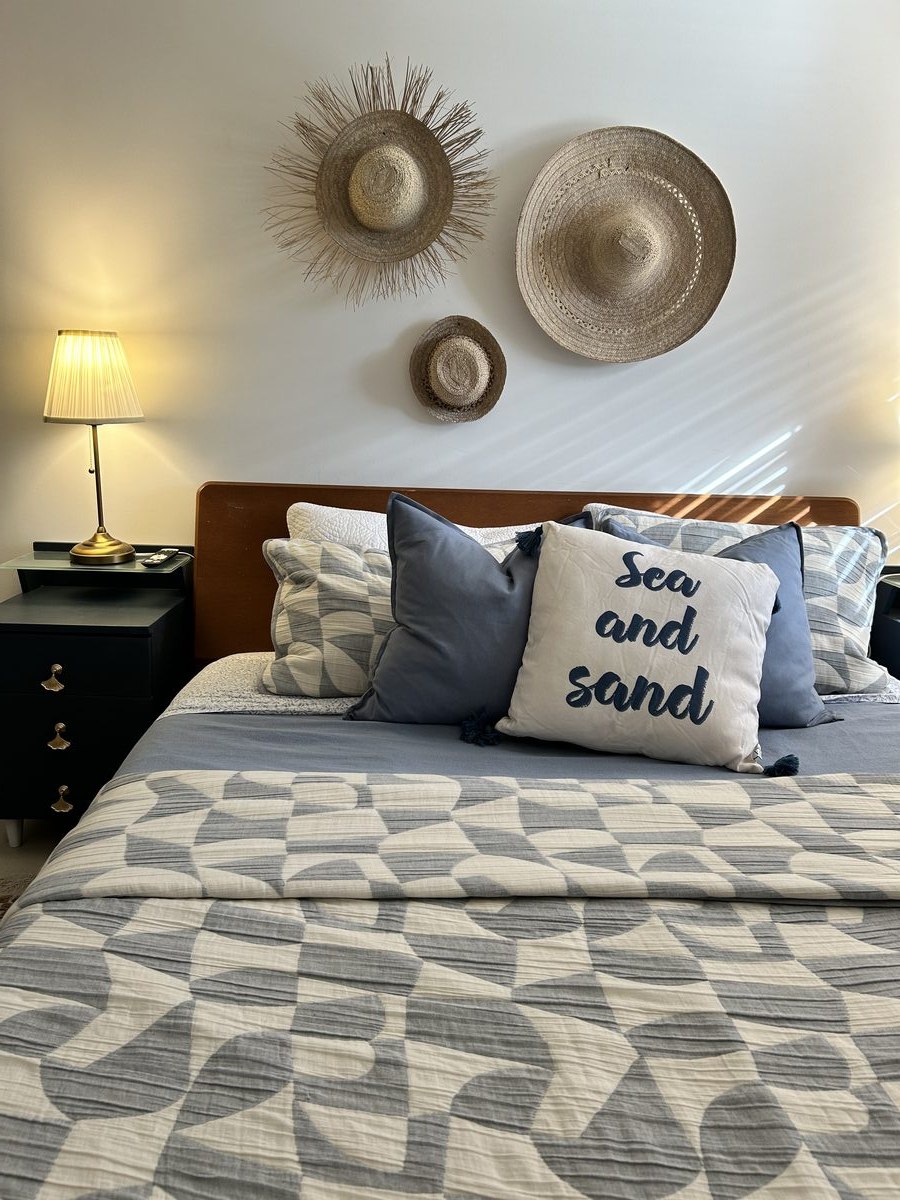 Coastal primary bedroom with a woven sun hat gallery wall and layered blue bedding