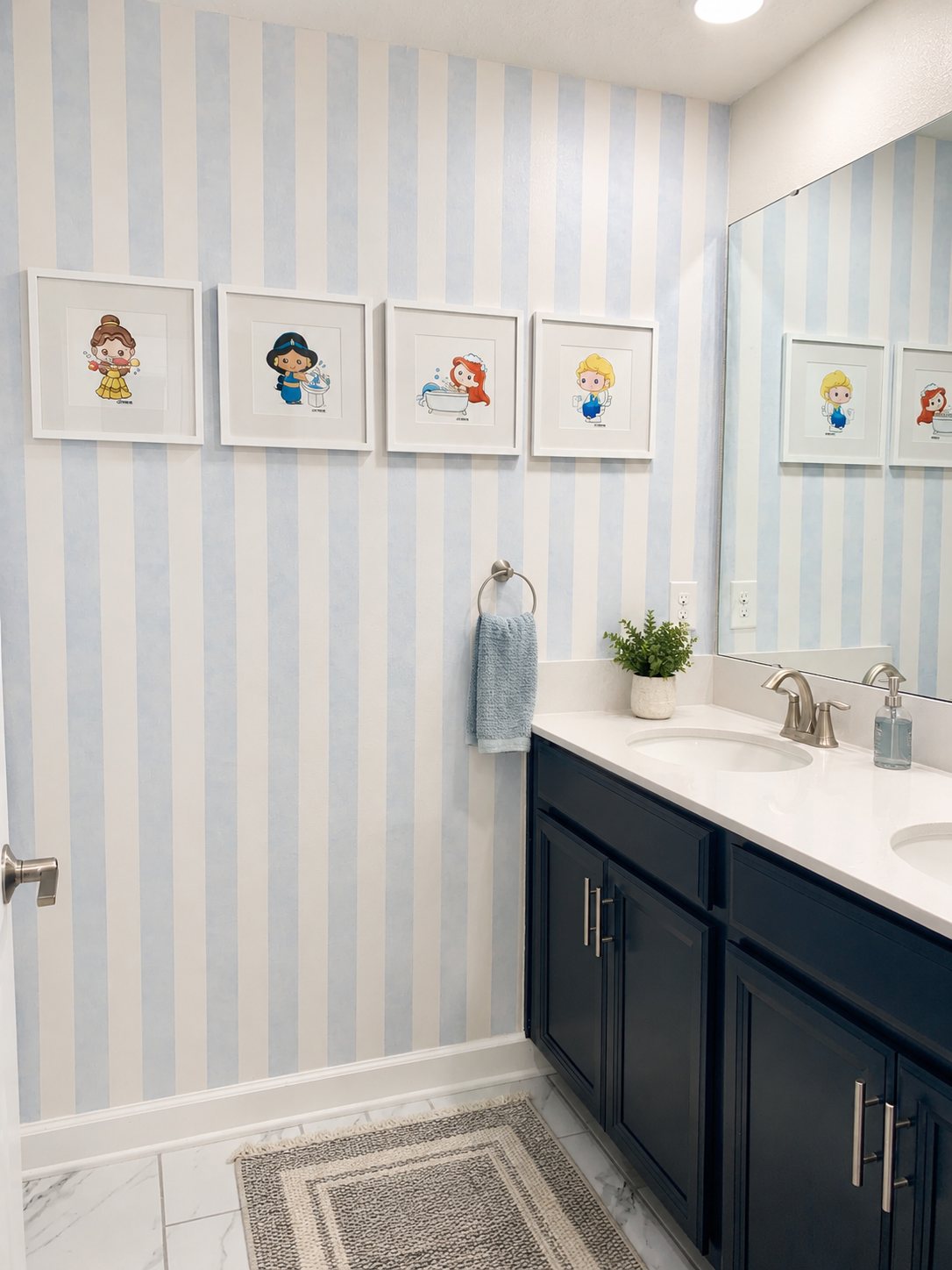 Kids bathroom with soft blue striped wallpaper, navy vanity and framed prints